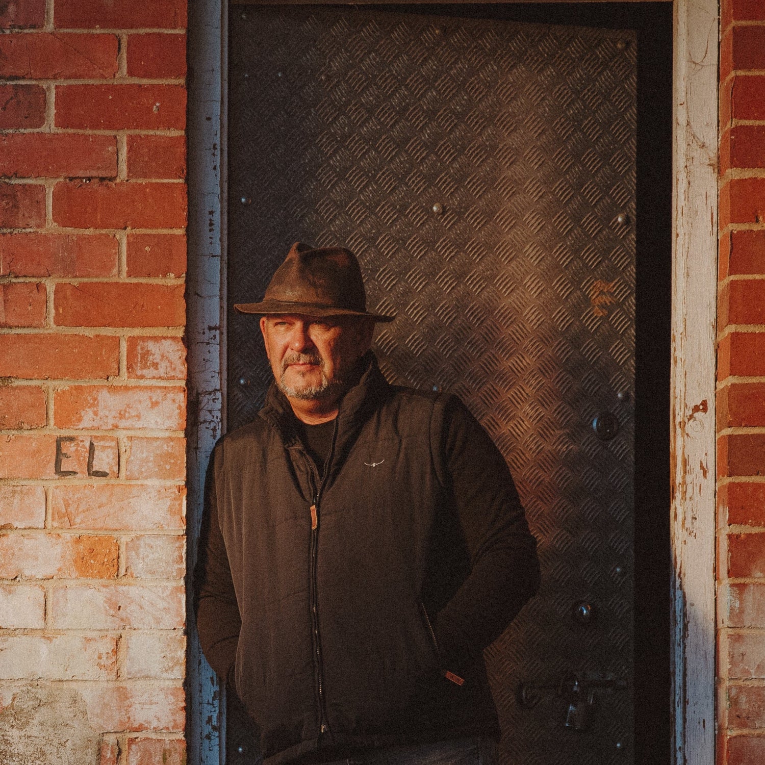Man standing in a doorway of a brick building with a clear sky.